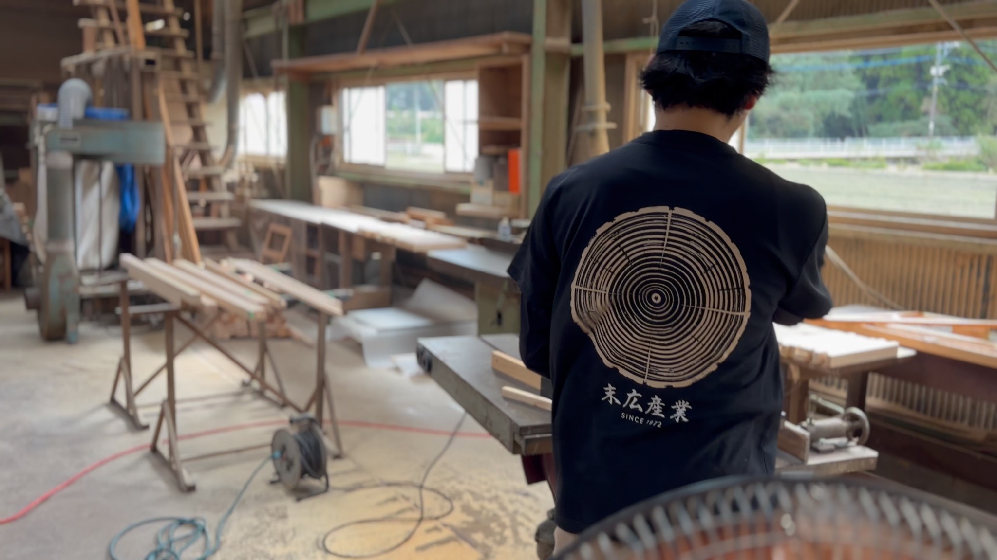 末広産業の制服を着た職人の後ろ姿と製材所